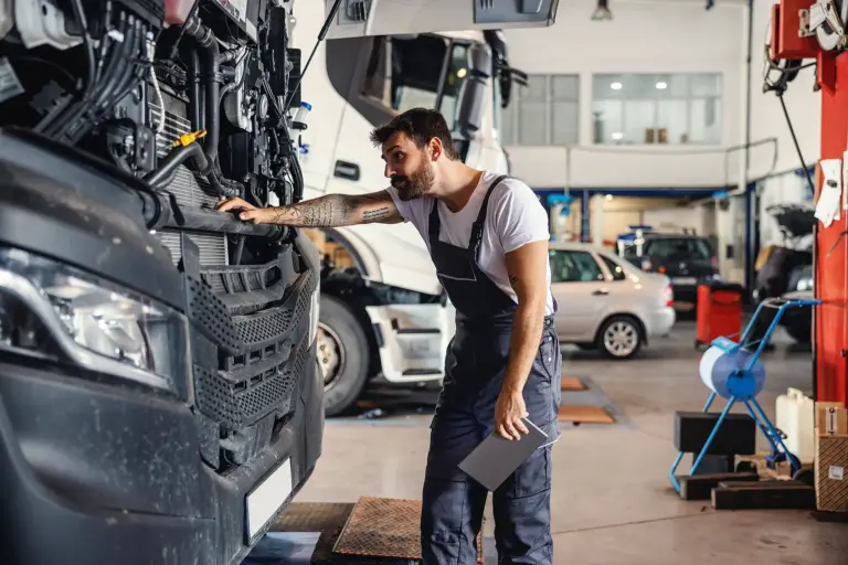 hardworking-tattooed-bearded-mechanic-leaning-truck-checking-motor-while-standing-garage-import-export-firm